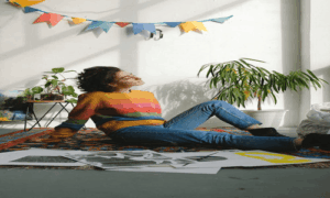 Invest in Your Own Happiness – woman relaxing on a rug with art prints, plants, and sunlight
